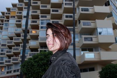 Portrait of young woman standing against building