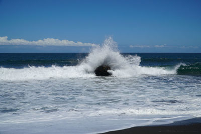 Waves splashing on shore against sky