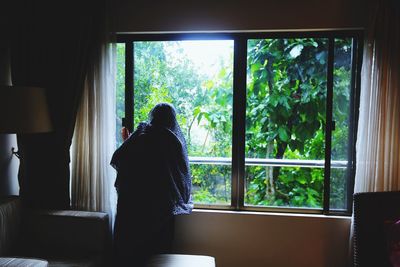 Rear view of woman looking through window at home