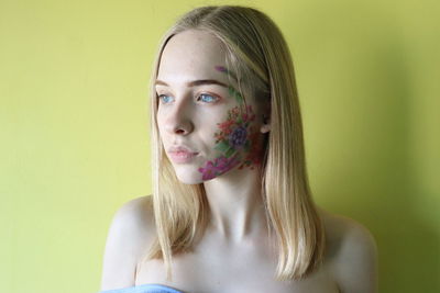 Young woman with painted face against yellow background