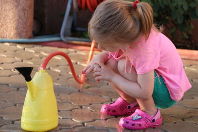 Full length of girl filling watering can with garden hose