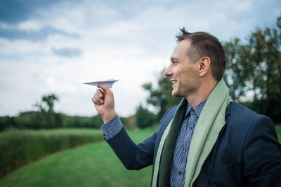 Businessman holding paper plane in green field