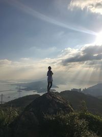 Rear view of woman standing on mountain against sky during sunny day