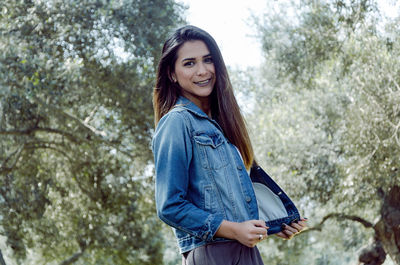 Portrait of smiling young woman standing against trees