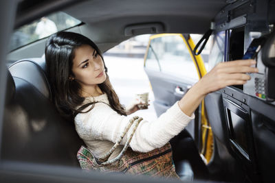 Young woman making contactless payment through smart phone in taxi