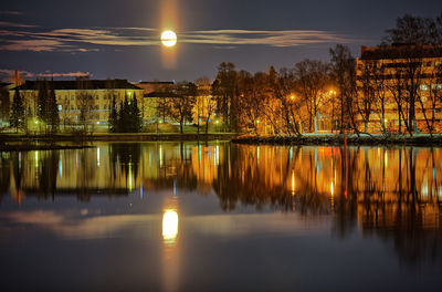 Illuminated buildings and full moon reflecting on calm lake