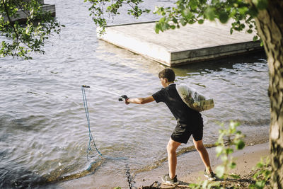 Full length rear view of boy picking up rope from lake on shore