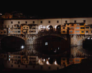 Arch bridge over river in town against sky at night