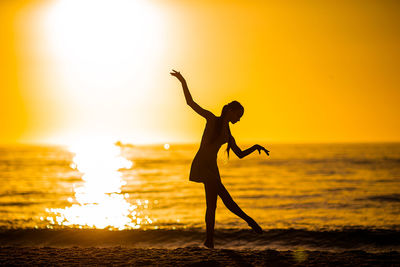 Silhouette woman doing yoga at beach against sky during sunset