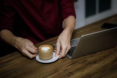 Midsection of man holding coffee cup on table