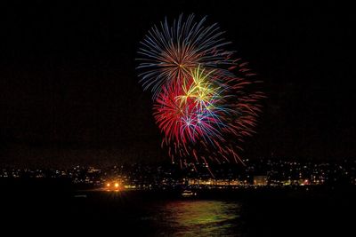 Low angle view of firework display over city and river at night