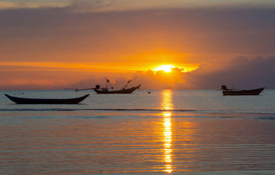 Silhouette people on sea against orange sky during sunset