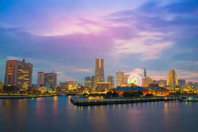 Illuminated buildings by river against sky in city