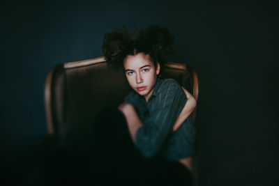 Portrait of a young woman sitting against black background