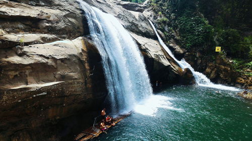 People by waterfall on wooden raft