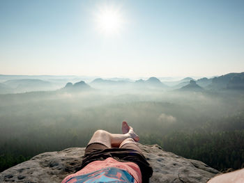 Low section of man relaxing on mountain against sky