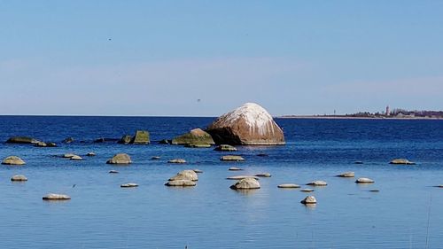 Rocks in sea against clear blue sky
