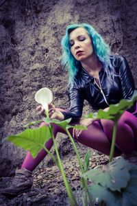 Portrait of young woman sitting on rock against trees