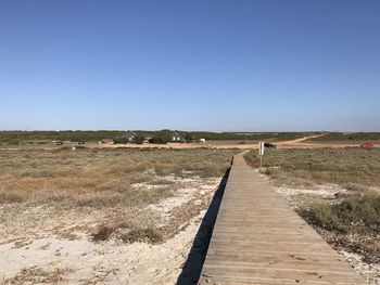 Footpath amidst field against clear blue sky