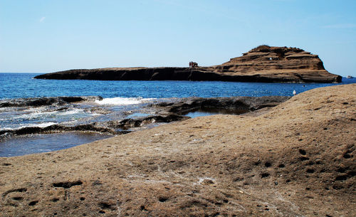 Rock formations on beach against clear blue sky