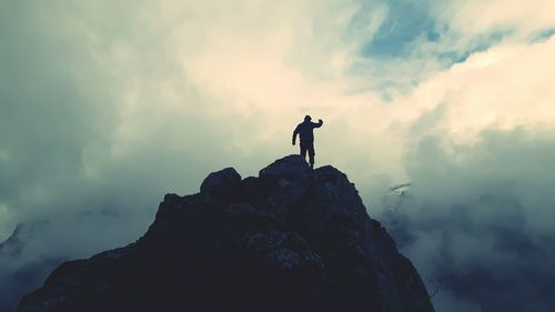 Rear view of man standing at the edge of cliff against cloudy sky