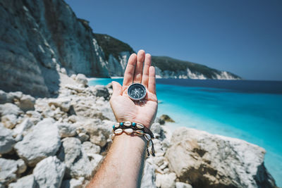 Midsection of person holding rock in sea against sky