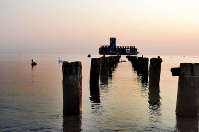 Wooden posts in sea against sky during sunset