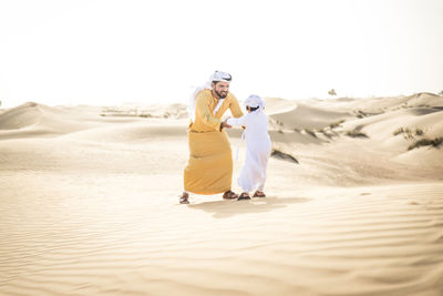 Rear view of couple on sand dune in desert against sky