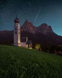 Lighthouse by buildings against sky at night