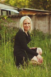 Portrait of young woman crouching on grassy field