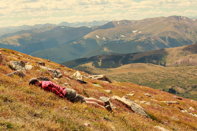 Mid adult man relaxing on mountains against cloudy sky