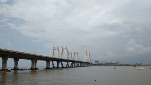 Bridge over calm river against cloudy sky