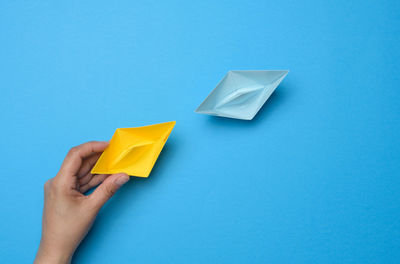 A woman's hand holds a yellow paper boat, next to it is blue. the concept of supporting independent