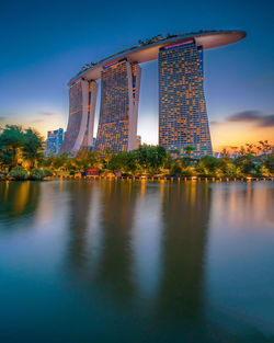 Illuminated building by river against sky