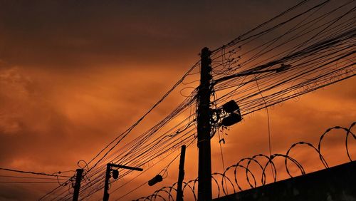 Low angle view of electricity pylon against sky during sunset