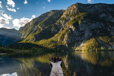 People on lake by mountains against sky