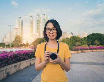 Portrait of smiling young woman holding camera in city