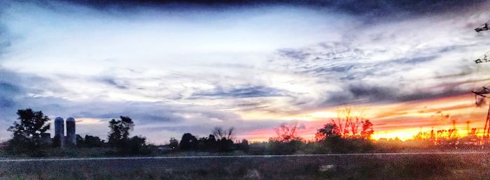 Silhouette trees on field against dramatic sky