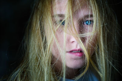 Close-up portrait of teenage girl with tousled hair against black background