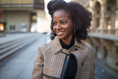Beautiful african american young woman with afro and large hoop earrings in a stylish coat, smiling