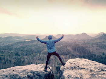 Happy man in blue sweatshirt with raised arms gesture triumph on exposed cliff. crazy hiker on peak