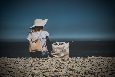 Man sitting on pebbles at beach against sky