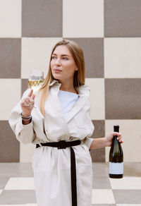 Young woman tasting white wine against chessboard background