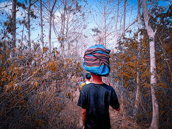 Rear view of woman standing by trees in forest