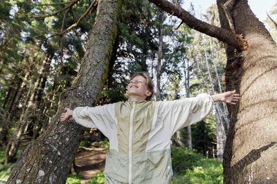 Smiling girl with arms outstretched standing amidst tree trunks