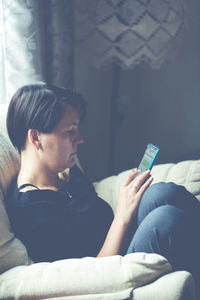 Side view of mature woman using smart phone on sofa at home