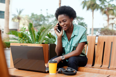 Young woman talking over mobile phone while using laptop at cafe