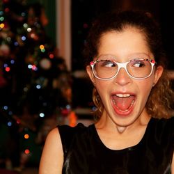 Excited woman with mouth open sideways glancing against christmas tree