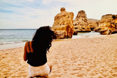 Rear view of woman standing on rock at beach against sky