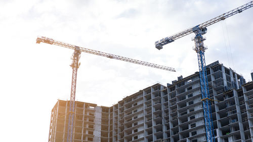 Low angle view of crane by building against sky